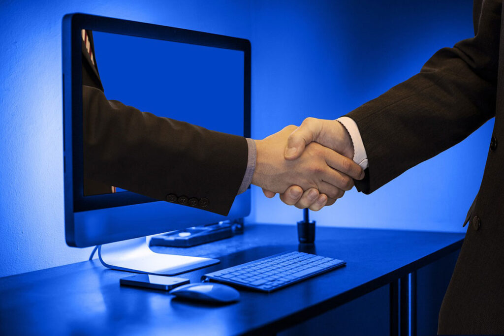 Two people shaking hands in front of a computer